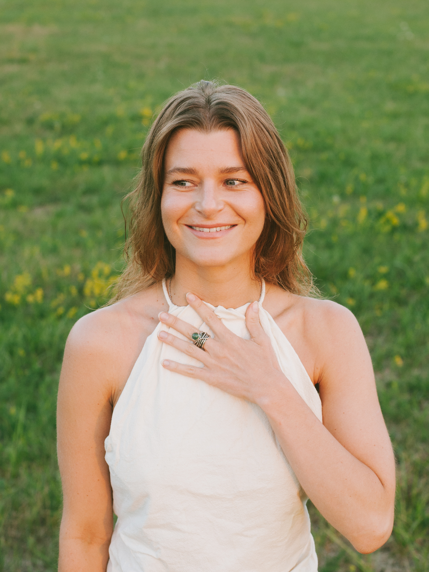 Viktória Kaslik smiling in a sunlit meadow, hand resting on her heart.