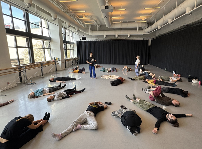Participants lying on the floor of a bright studio during a contact improvisation workshop.
