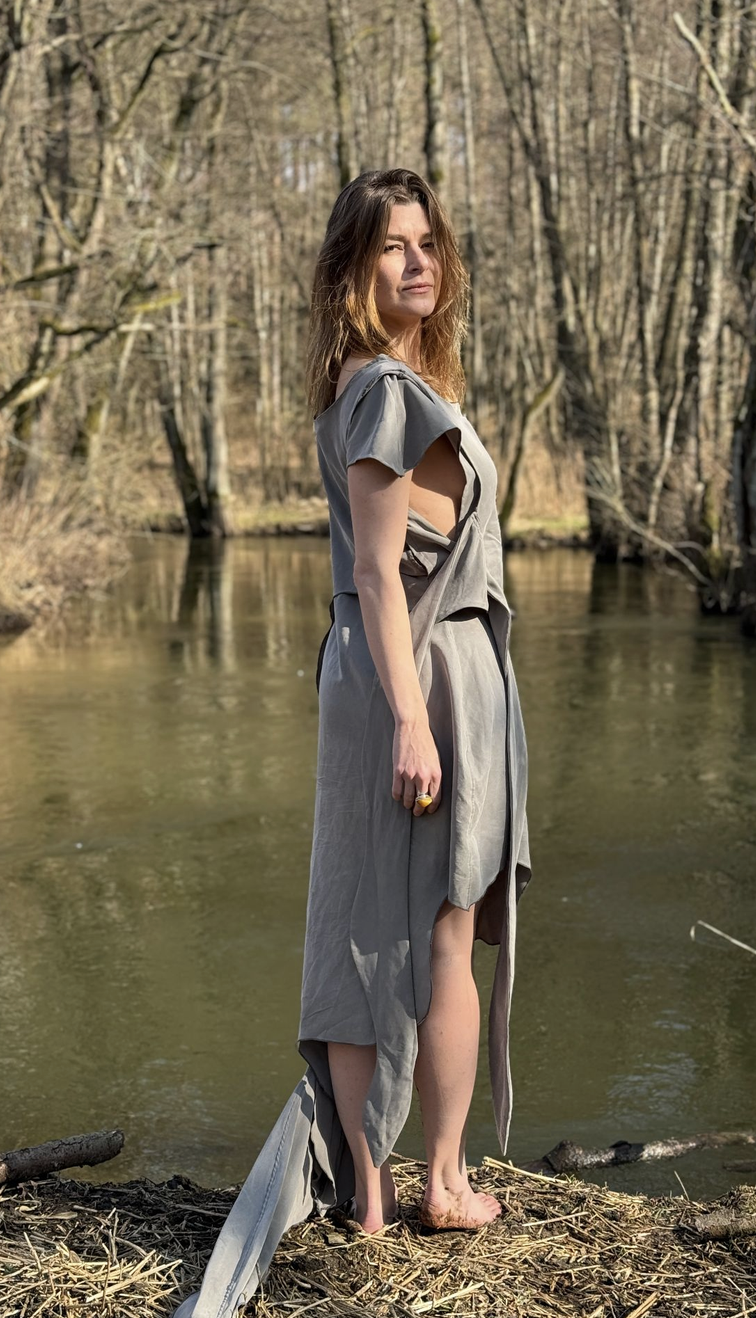Viktória wearing the grey Hecate legal costume beside a river in early spring.