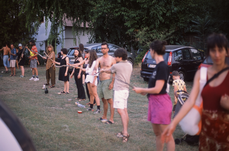 Participants standing in a long line passing poplar branches across the meadow.